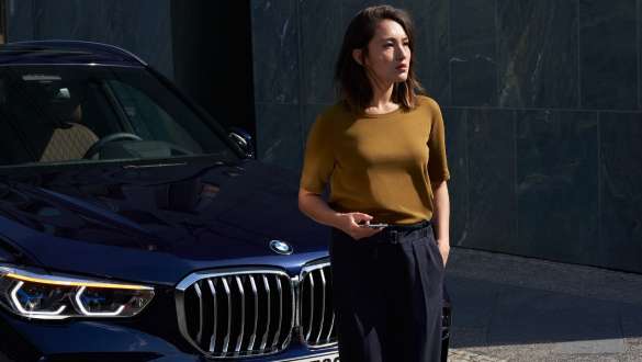 BMW Roadside Assistance. BMW Roadside Assistance woman with smartphone in front of a BMW