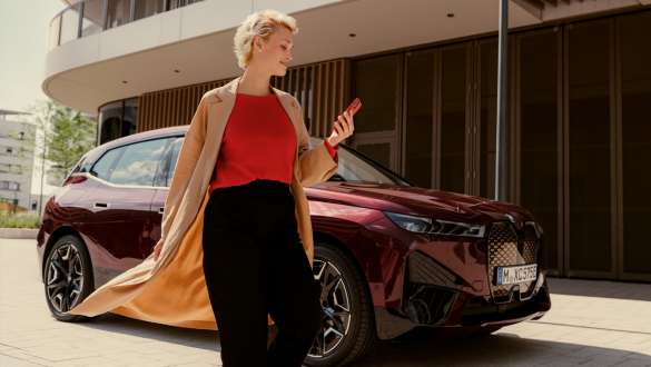 Walking woman in front of BMW iX uses My BMW app on smartphone Walking woman in front of BMW iX uses My BMW app on smartphone