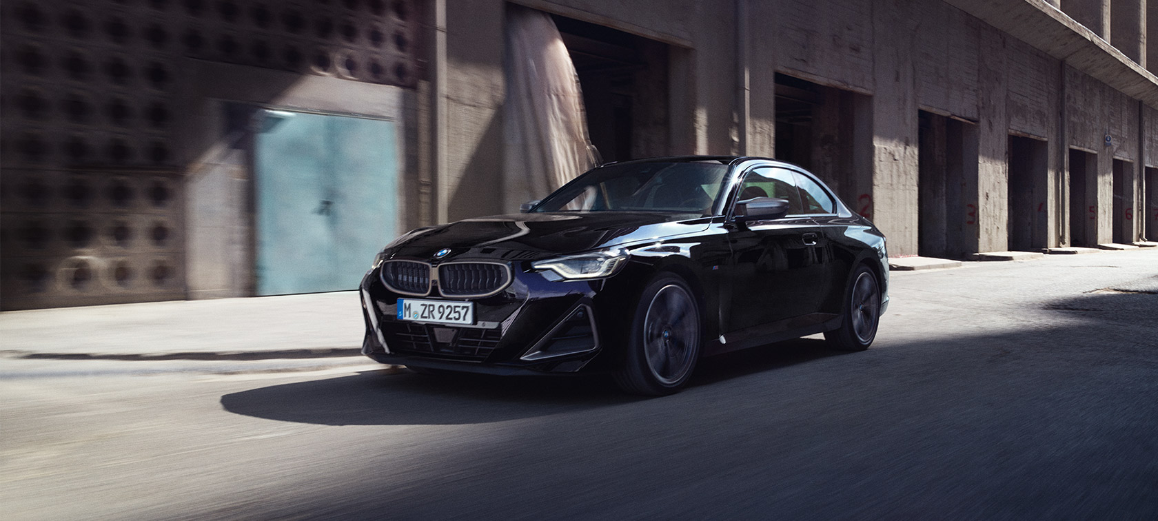 BMW M240i xDrive Coupé G42 2021 three-quarter front view driving BMW M240i xDrive Coupé G42 2021 Black Sapphire metallic three-quarter front view driving