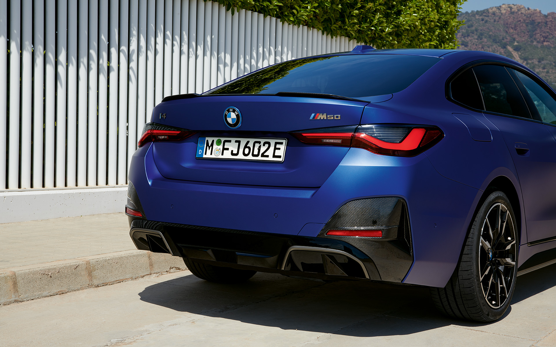 BMW i4 M50 G26 2021 BMW Individual Frozen Portimao Blue metallic three-quarter rear view standing by white fence