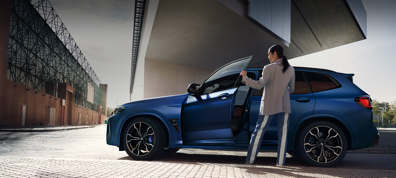 BMW X3 M F97 LCI Facelift 2021 side view standing BMW X3 M F97 LCI Facelift 2021 BMW Individual Frozen Portimao Blue metallic side view standing with open door and female model