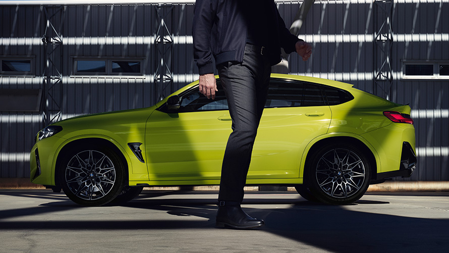 Model in front of side view BMW X4 M Competition F98 LCI Facelift 2021 BMW X4 M Competition F98 LCI Facelift 2021 BMW Individual Sao Paulo yellow side view with model