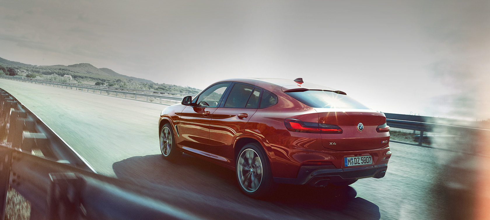 BMW X4 driving on the road BMW X4 M40i G02 2018 Flamenco Red brilliant effect three-quarter rear view driving on the road