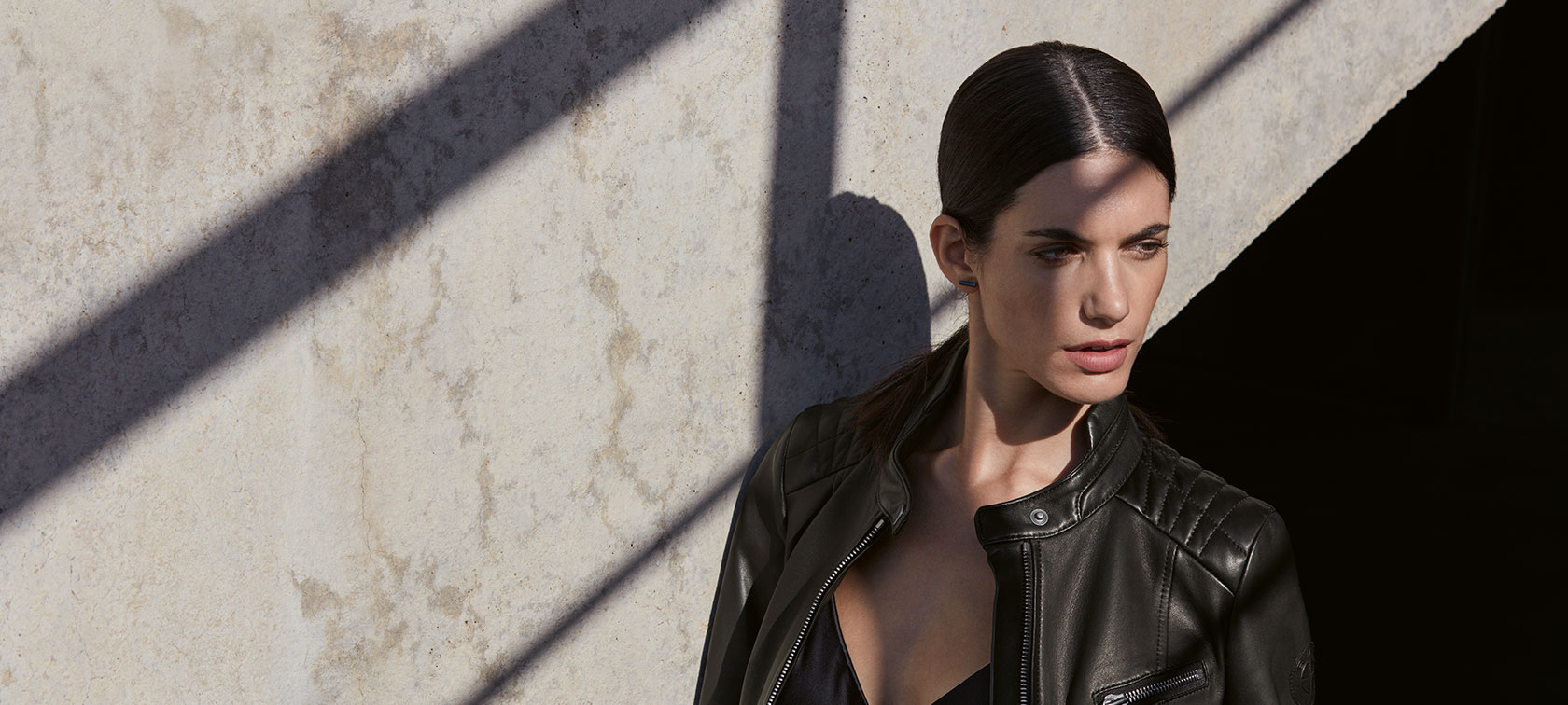 Defining Life and Style. In the picture, a young woman is wearing the BMW Ladies Leather Jacket in front of an urban backdrop.