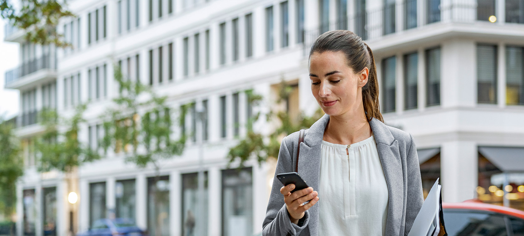 Woman standing in front of building looking at her smartphone Remote Software Upgrade Woman standing in front of building looking at her smartphone