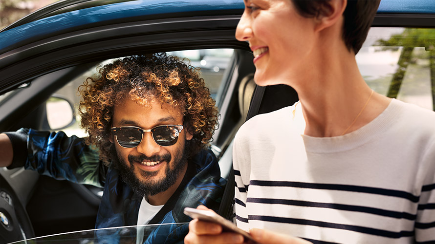 BMW Connected Man in BMW and woman outside the BMW using BMW Connected on smartphone