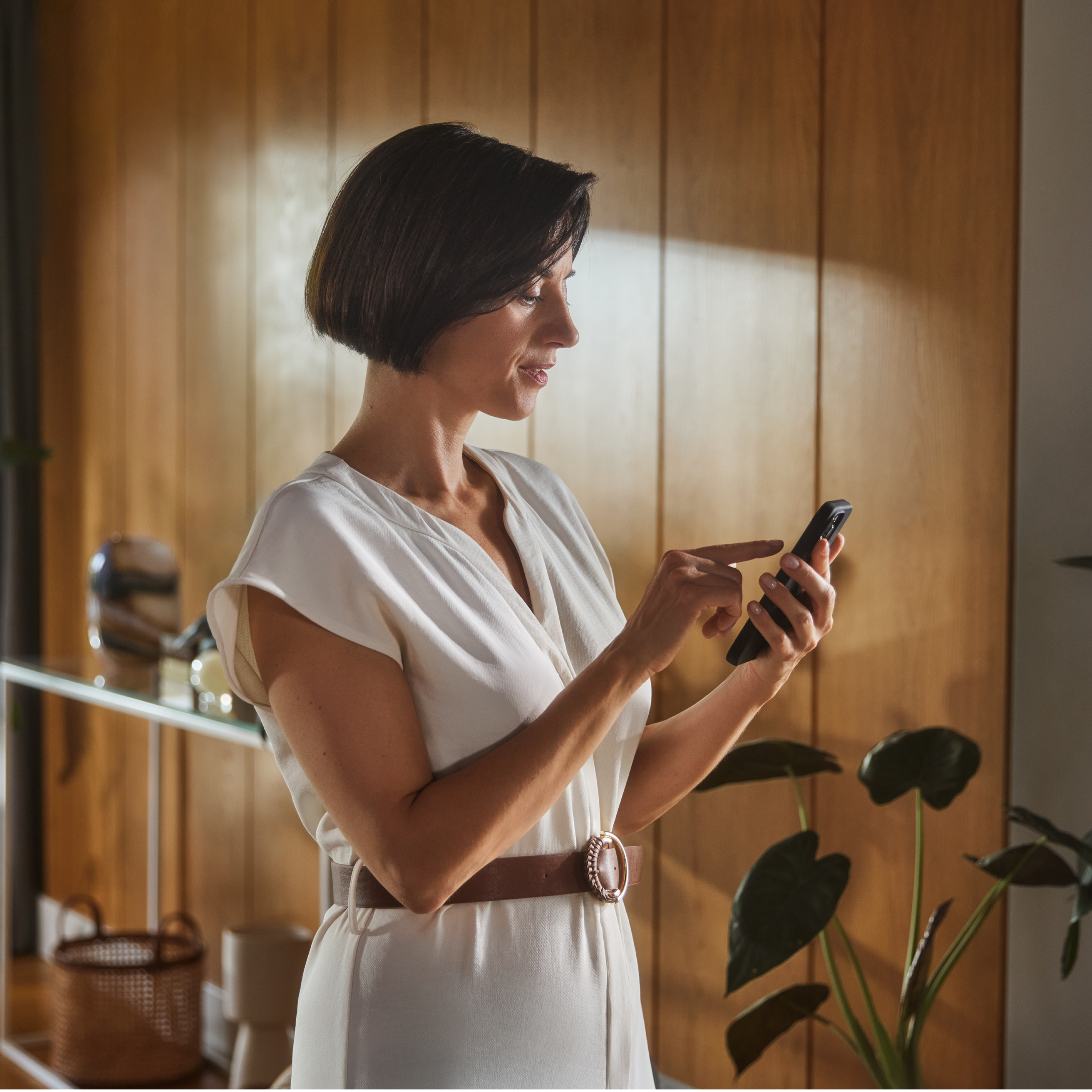 A woman is looking at her smartphone, a wallbox is visible in the background
